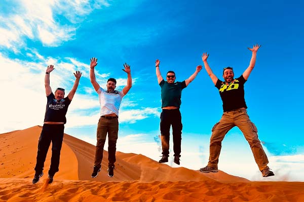 Todo el grupo congelado en el aire saltando en una duna en el desierto del Sáhara, Marruecos